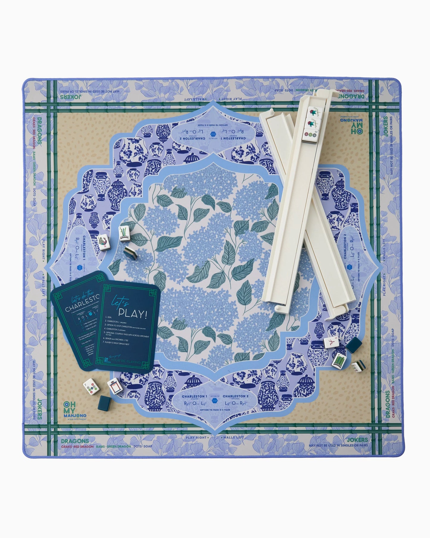Oh My Mahjong instructional Mahjong Mat with French blue hydrangeas, chinoiserie ginger jars and ginkgo leave pattern and antelope animal patter in tan with bamboo border with white mahjong rack, navy shufflers and Gatsby tiles