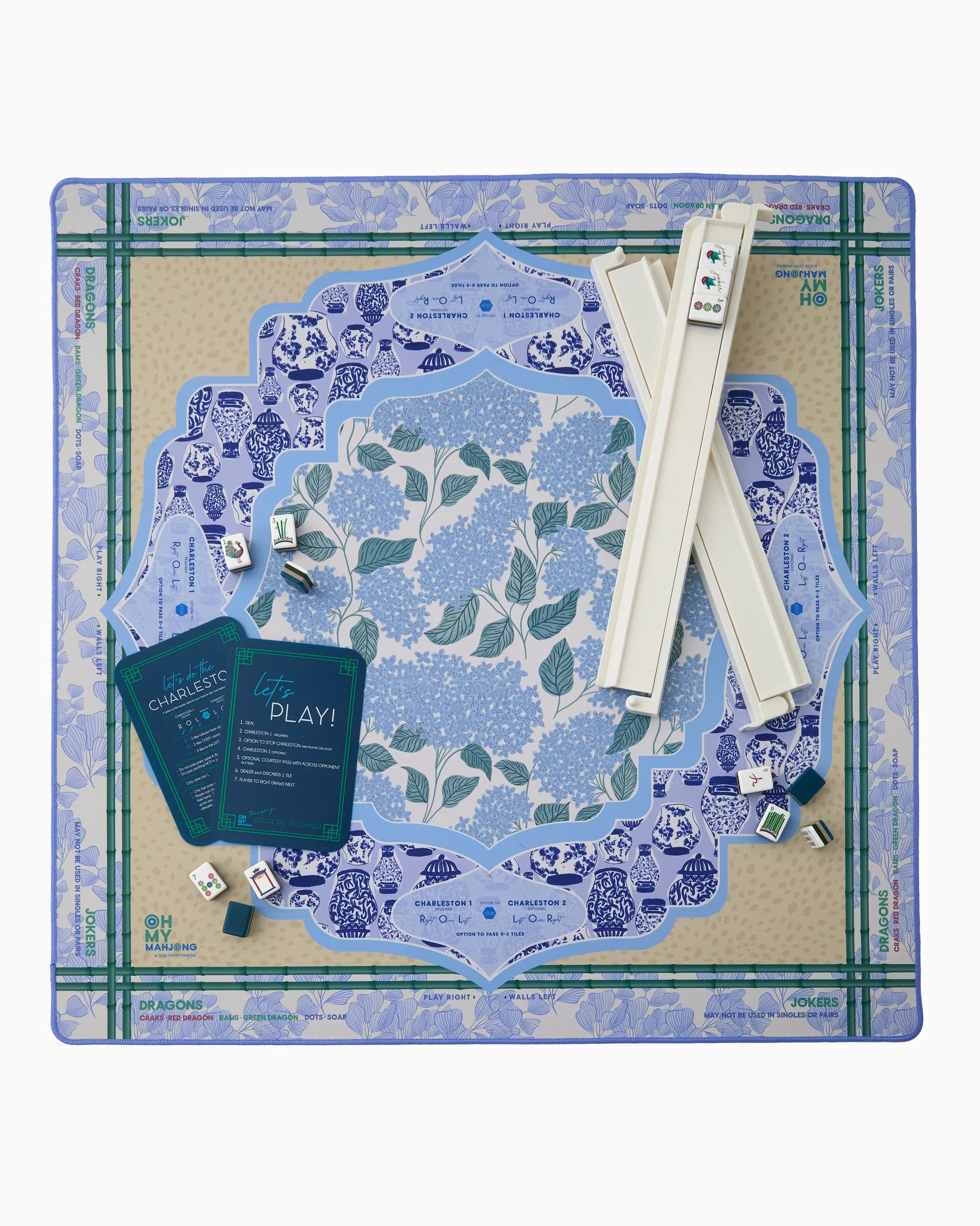 Oh My Mahjong instructional Mahjong Mat with French blue hydrangeas, chinoiserie ginger jars and ginkgo leave pattern and antelope animal patter in tan with bamboo border with white mahjong rack, navy shufflers and Gatsby tiles